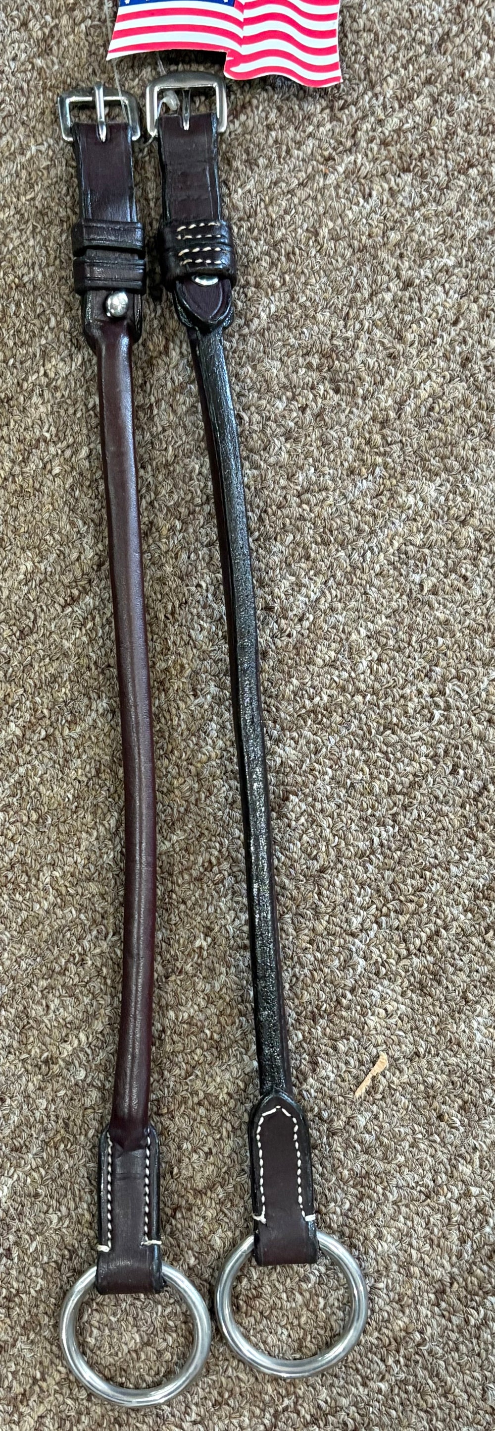 Two leather straps with metal rings on a textured surface