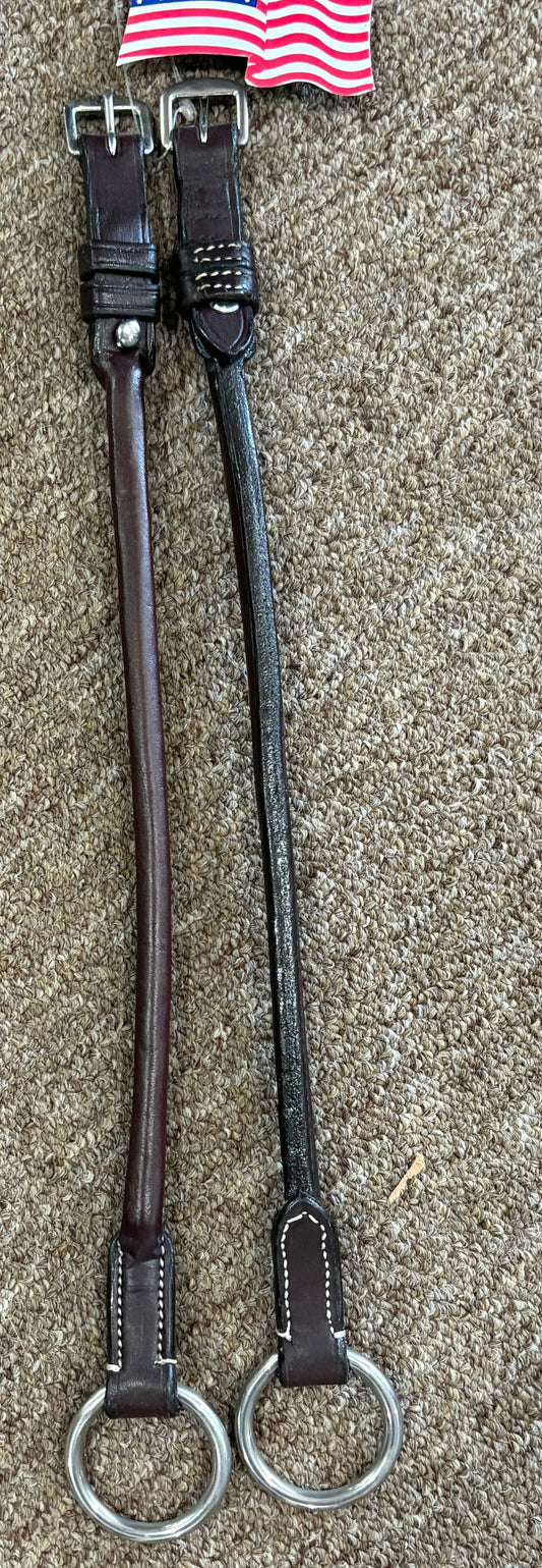 Two leather straps with metal rings on a textured surface