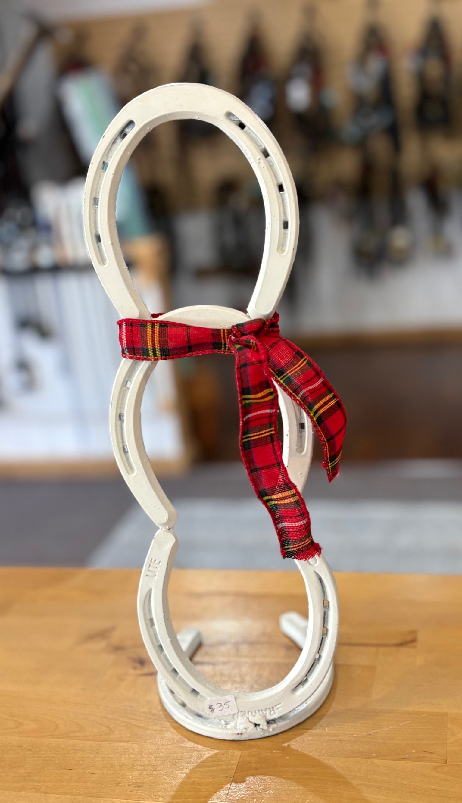 Decorative snowman made from white horseshoes with a red plaid ribbon on a wooden surface.
