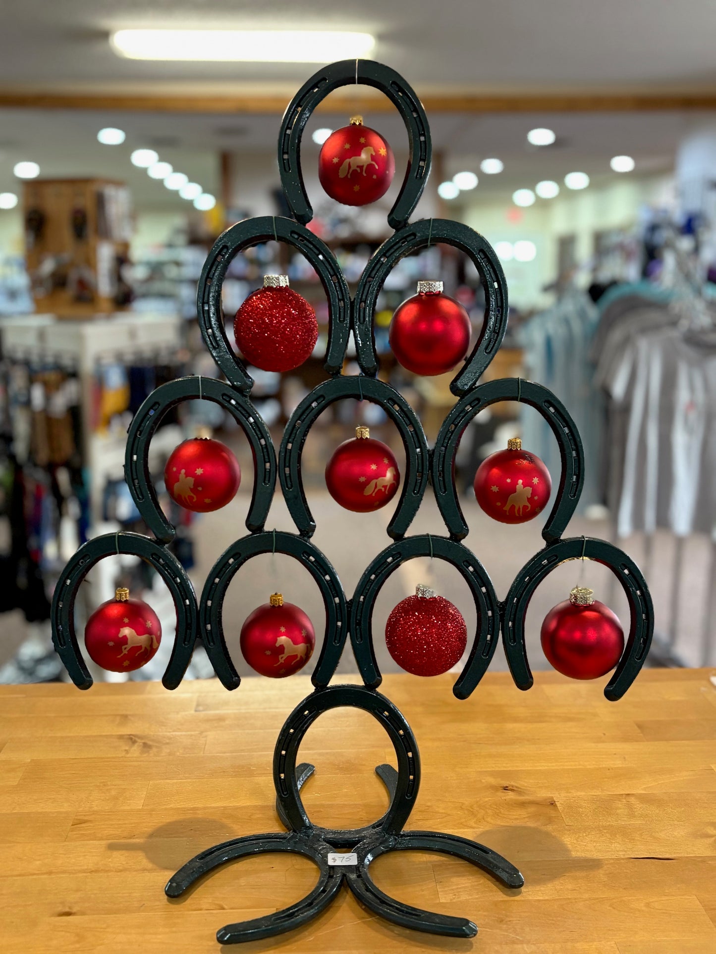 Decorative tree made of horseshoes with red ornaments on a wooden surface.
