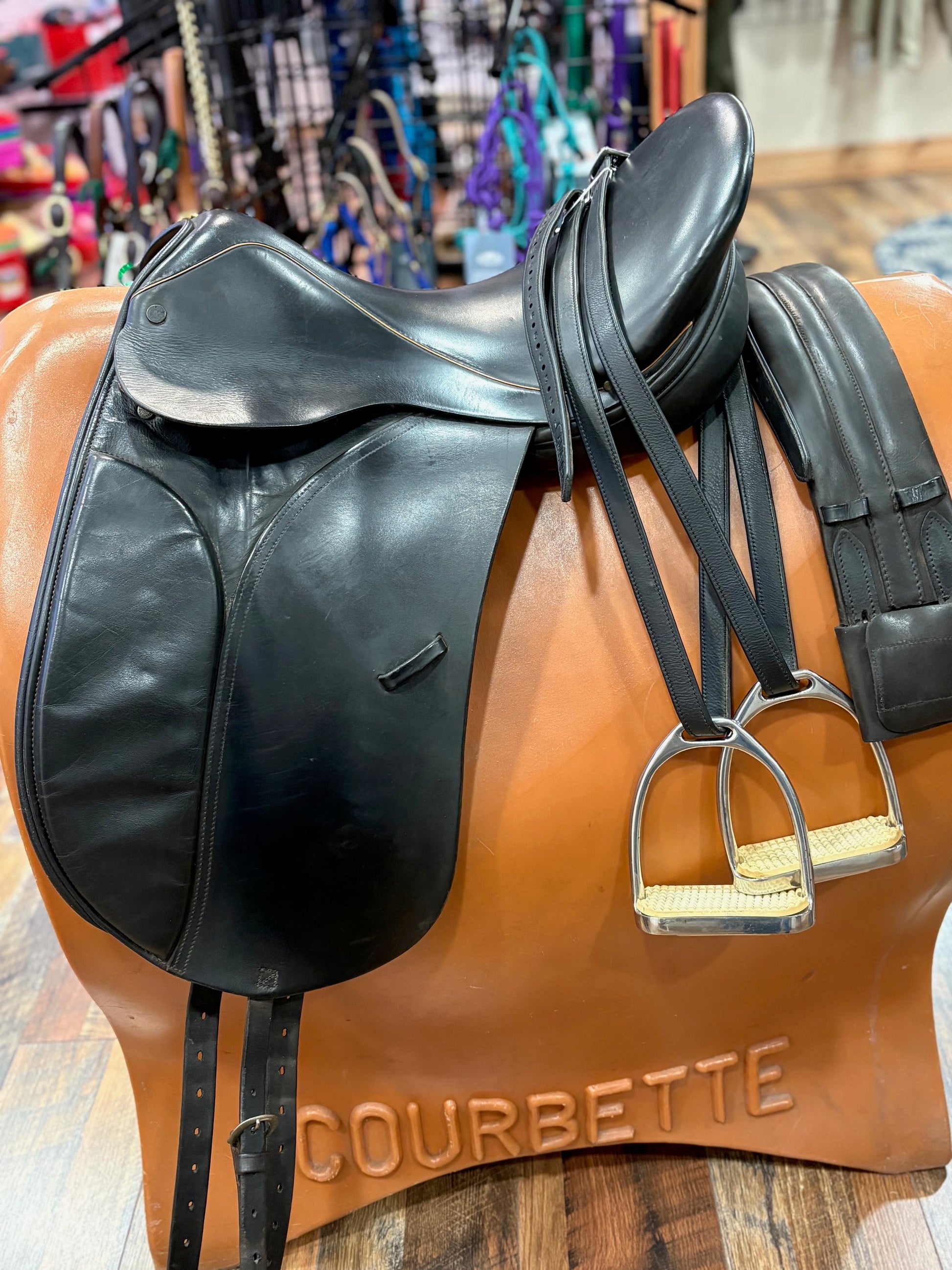 Black dressage saddle shown with a pair of stirrups on leathers and a leather girth