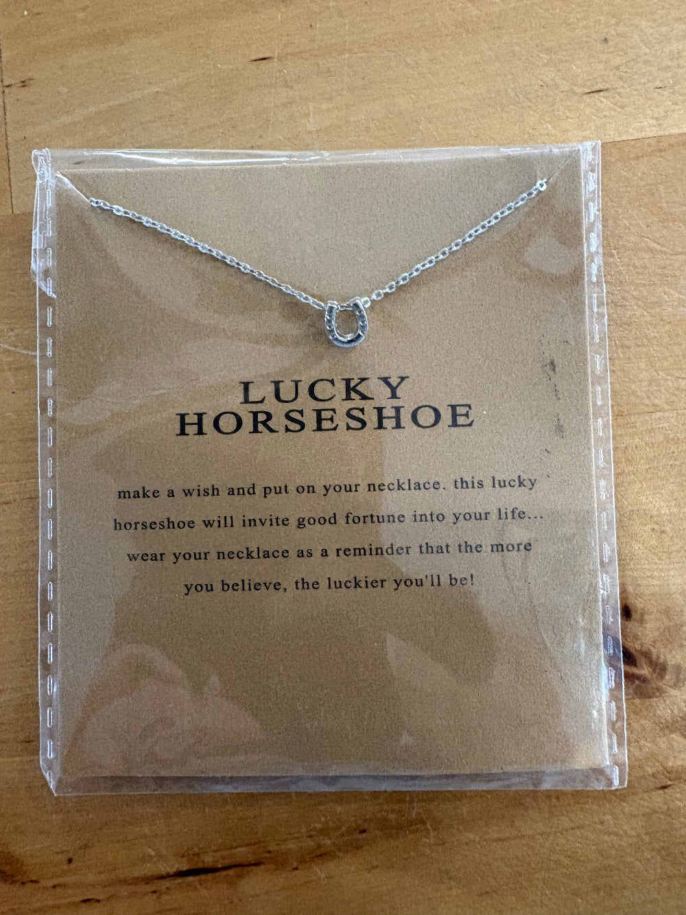 Silver horseshoe necklace on a card with text on a wooden surface