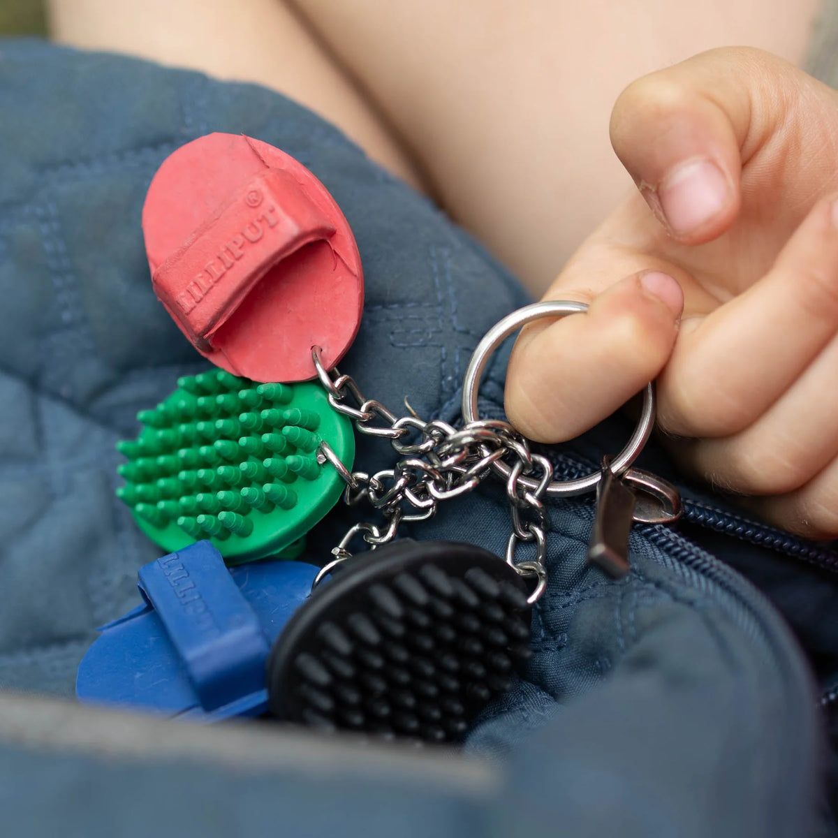 Keychain with colorful rubber curry comb charms held by a hand against a blue fabric background