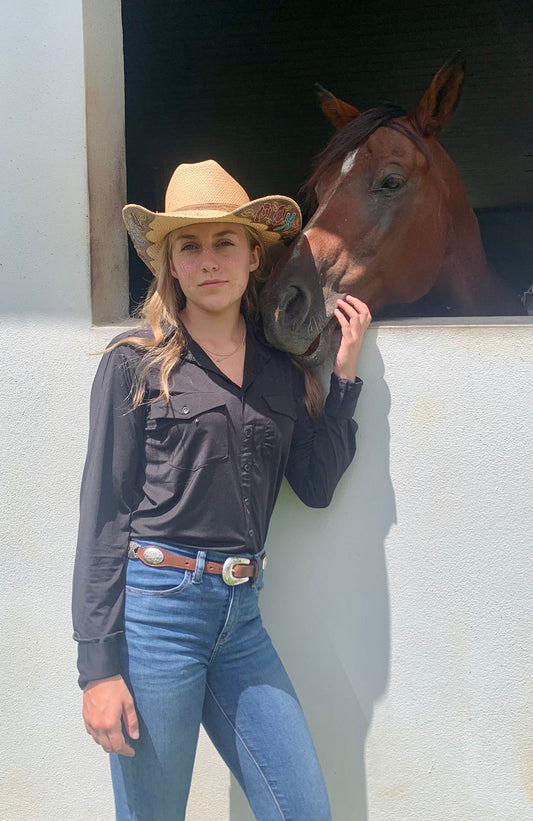 women standing next to horse wearing black long sleeve equestrian button down shirt with two pockets on chest, with blue jeans and brown belt