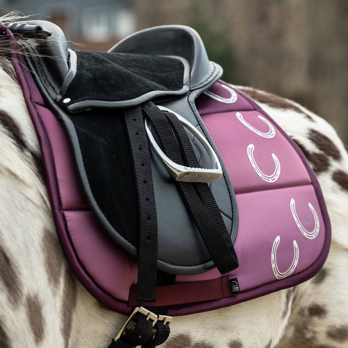 Lilac colored saddle pad shown on a spotted horse with a black saddle