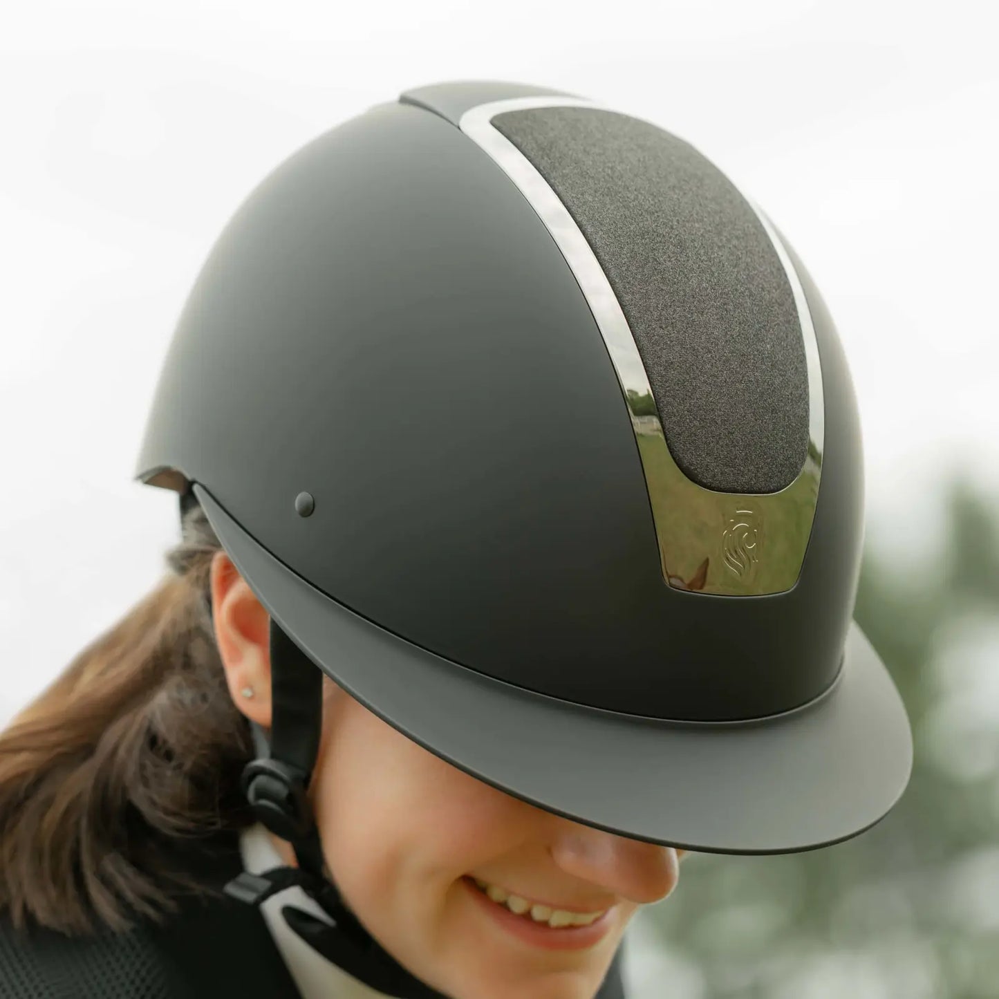 Person wearing a black riding helmet with a touch of chrome and subtle sparkle.