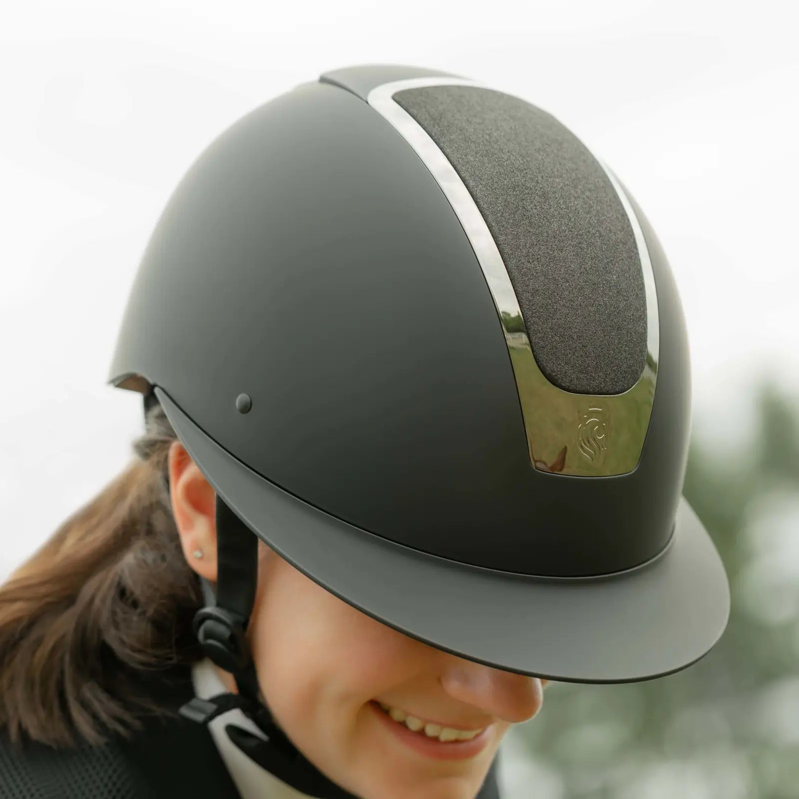 Person wearing a black riding helmet with a touch of chrome and subtle sparkle.