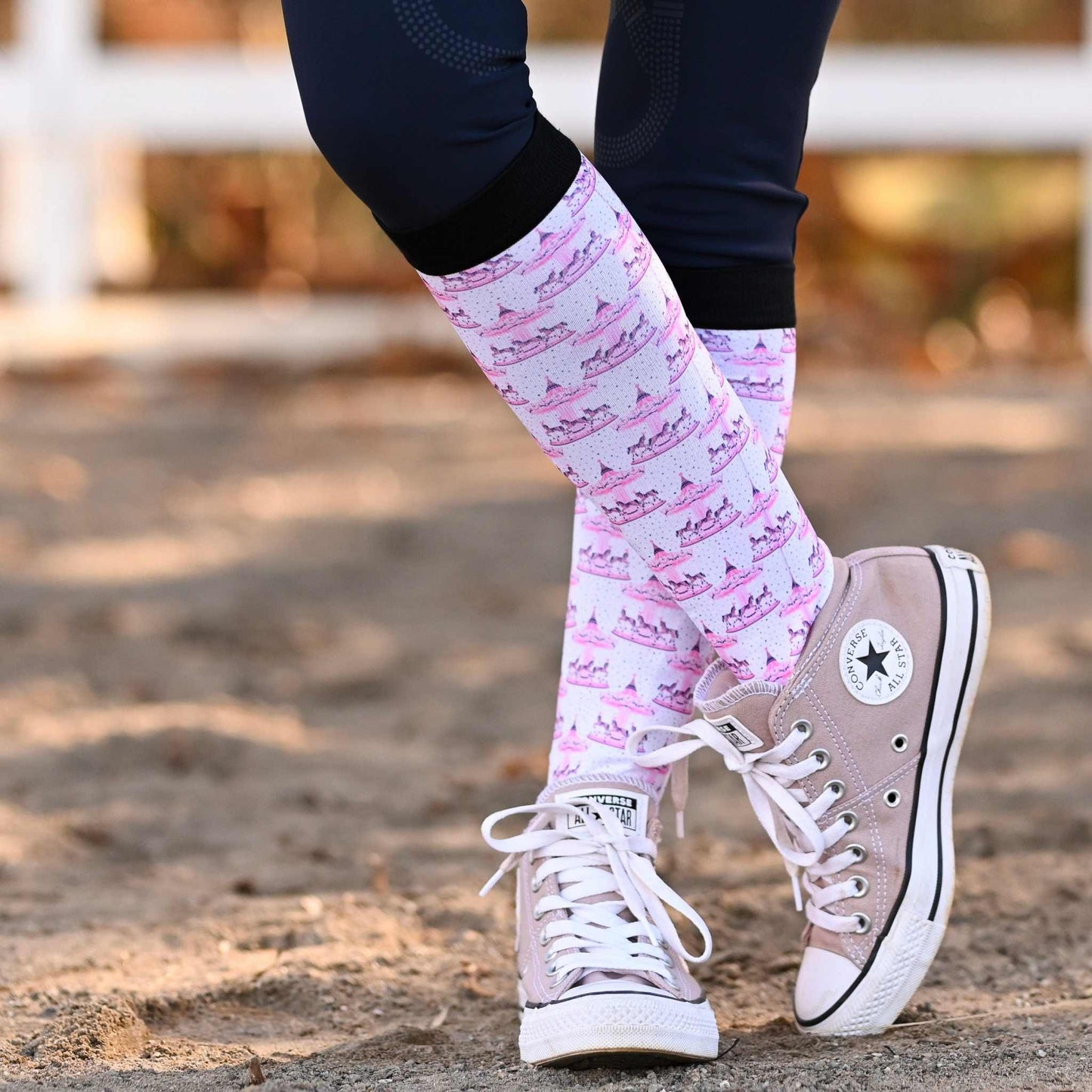 Person wearing pink patterned socks and beige Converse sneakers on a blurred outdoor background