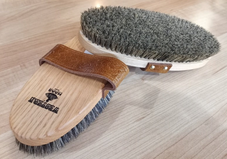 Front and back of a wooden equine grooming brush with a leather handle