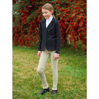 Young equestrian girl wearing a dark show jacket, tan jodhpurs and dark paddock boots.